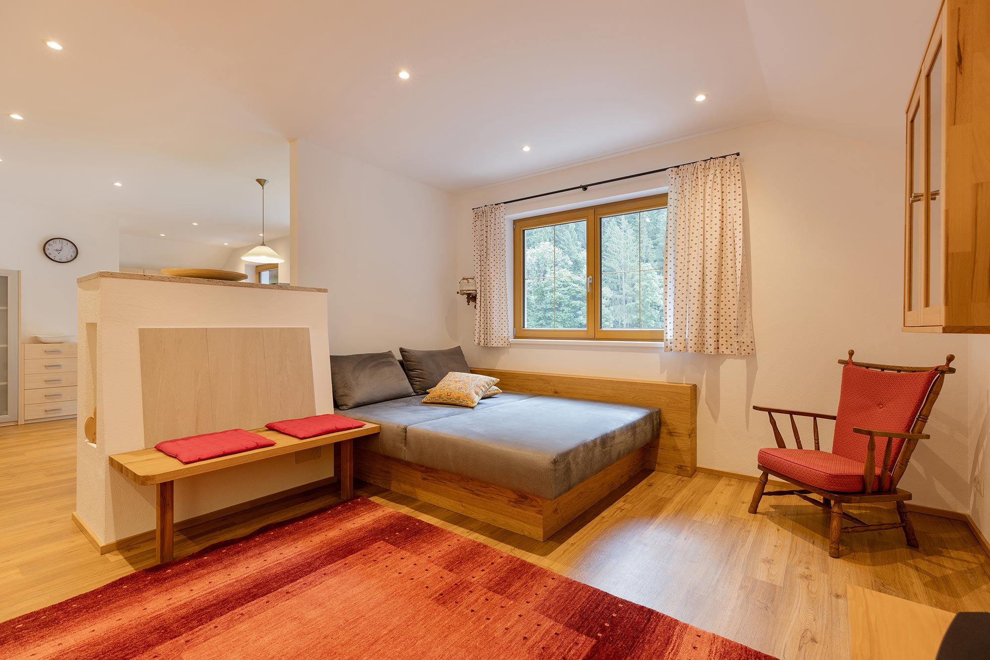 Gemütliche Kuschelliege im Wohnzimmer mit Kachelofen und  Blick auf Wiese, Wald und Berge.